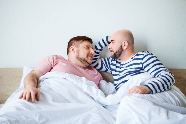 Un par de hombres acostados uno al lado del otro en la cama, pasando tiempo de calidad juntos. - Foto, imagen