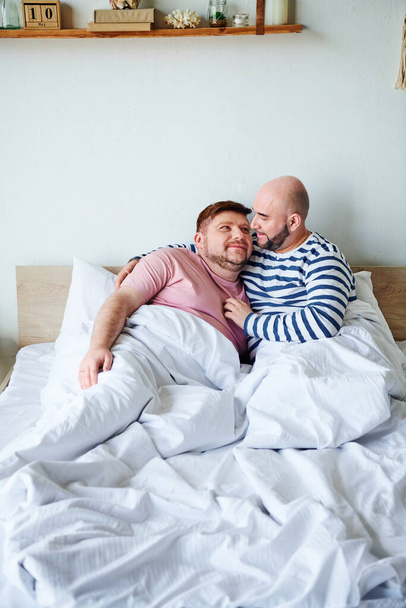Δύο άνδρες χαλαρώνουν σε ένα κρεβάτι στο σπίτι τους - Φωτογραφία, εικόνα