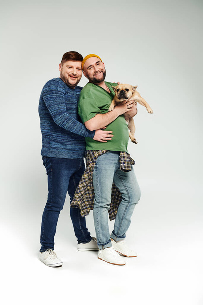 A loving gay couple standing together, holding a French bulldog. - Photo, Image