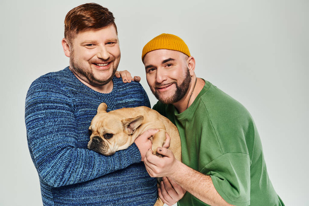 İki adam şefkatle kucağında küçük bir Fransız Bulldog 'u tutuyor.. - Fotoğraf, Görsel
