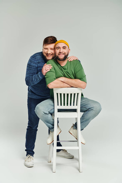 Due uomini che si abbracciano affettuosamente su una sedia, mostrando amore e insieme in un momento intimo. - Foto, immagini