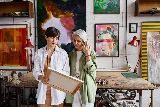 A mature lesbian couple examining painting in studio. - Photo, image