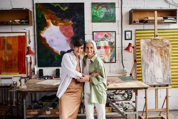 Two mature women, a lesbian couple, stand side by side in an art studio. - Фото, зображення