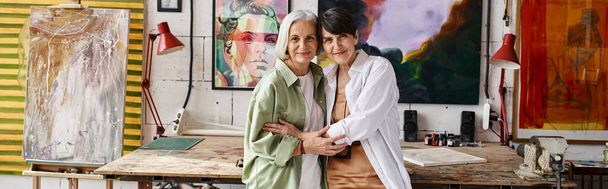 Two mature women, a couple, standing stylishly together in an art studio. - Photo, image