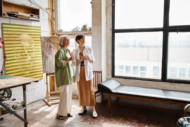 Due donne mature che condividono un momento di cameratismo in un vibrante studio d'arte. - Foto, immagini