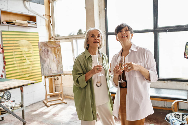 Two mature women, a loving couple, stand side by side in an art studio. - Fotoğraf, Görsel