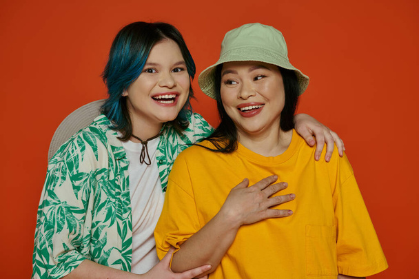 Eine asiatische Mutter und ihre Teenager-Tochter posieren elegant für ein Foto in einem Studio vor orangefarbenem Hintergrund. - Foto, Bild