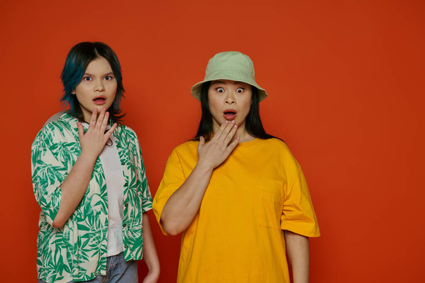 Een moeder en haar tienerdochter, beide Aziatisch, staan zij aan zij in een studio tegen een oranje achtergrond. - Foto, afbeelding