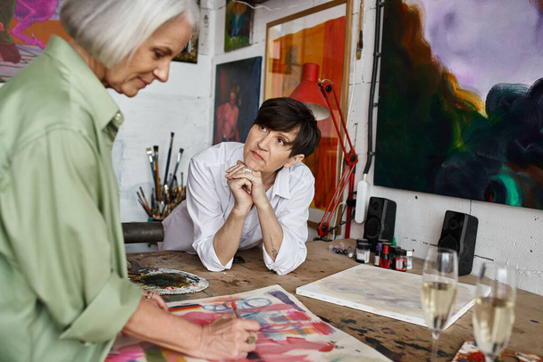 A woman is seated at a table in front of a captivating painting in an art studio. - Foto, Imagem