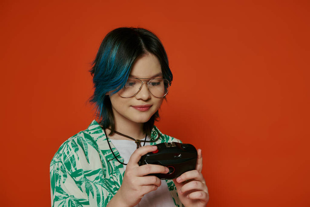 Una ragazza adolescente con i capelli azzurri vivaci in un ambiente di studio, con una fotocamera con uno sfondo arancione. - Foto, immagini