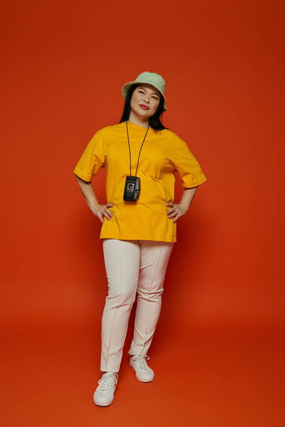 Eine Asiatin posiert gemeinsam in einem Studio und zeigt ihr stylisches gelbes Hemd und ihre weiße Hose vor orangefarbenem Hintergrund. - Foto, Bild