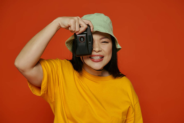 Азіатська жінка робить знімок, використовуючи ретро-камеру на помаранчевому фоні. - Фото, зображення