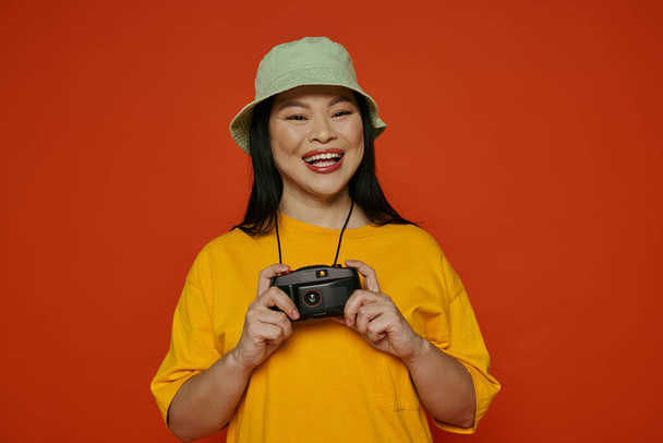 Una mujer asiática sostiene felizmente una cámara, sonriendo al espectador, en un estudio - Foto, Imagen