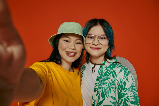 Azjatka i jej nastoletnia córka robią selfie w studio na pomarańczowym tle. - Zdjęcie, obraz
