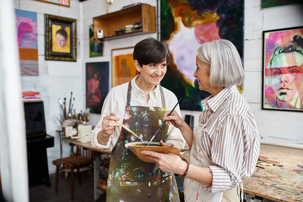 Δύο μεγαλύτερες γυναίκες δημιουργούν τέχνη σε ένα άνετο στούντιο. - Φωτογραφία, εικόνα