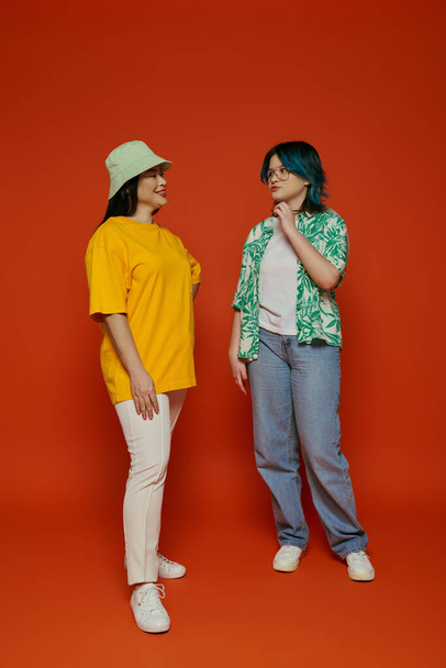 An Asian mother and her teenage daughter stand side by side in a studio against an orange background. - Photo, Image