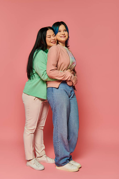 カジュアルな服装のアジアの母と十代の娘は活気に満ちたピンクの背景に一緒に立って,接続と団結を放射します. - 写真・画像