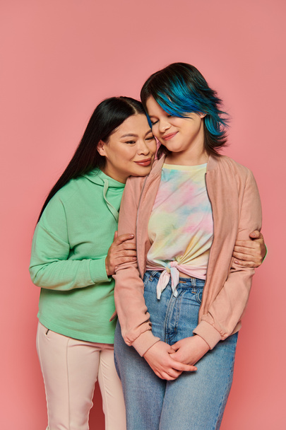 Duas mulheres, mãe asiática e sua filha adolescente, ficam ao lado uma da outra em roupas casuais contra um fundo rosa vibrante.. - Foto, Imagem