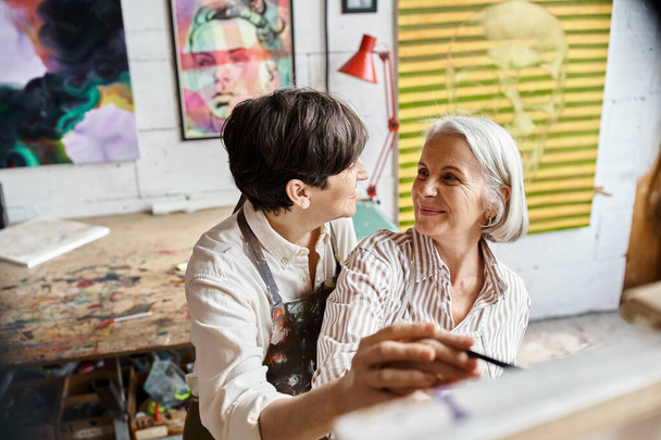 Two women engrossed in viewing an exquisite painting in an art studio. - Photo, Image