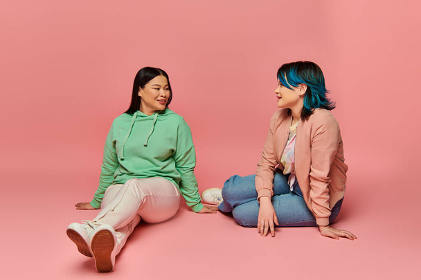 Eine asiatische Mutter und ihre Tochter im Teenageralter in lässiger Kleidung, auf dem Boden sitzend, in ein tiefes Gespräch verwickelt. - Foto, Bild