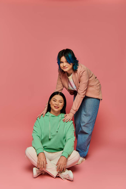 Eine Mutter und ihre Teenager-Tochter posieren gemeinsam vor einem leuchtend rosafarbenen Hintergrund in einem Studio-Setting. - Foto, Bild