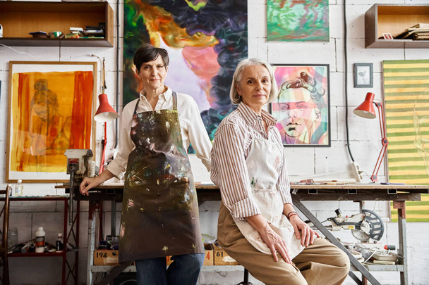 A mature lesbian couple standing in an art studio together. - Foto, afbeelding