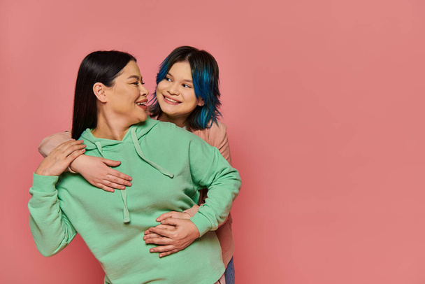 Een sereen moment vastgelegd als een Aziatische moeder en haar tienerdochter staan elegant naast elkaar in een studio setting. - Foto, afbeelding