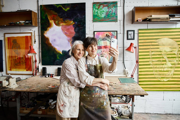 Two mature women, a couple, standing together in an art studio. - Photo, Image