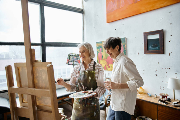 Two women, mature and in love, stand together in an art studio. - Photo, Image