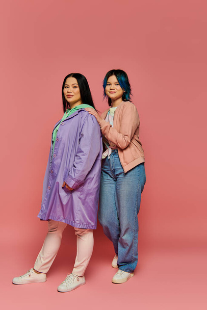 Азиатская мать и дочь-подросток стоят вместе, излучая любовь и силу перед ярким розовым фоном. - Фото, изображение