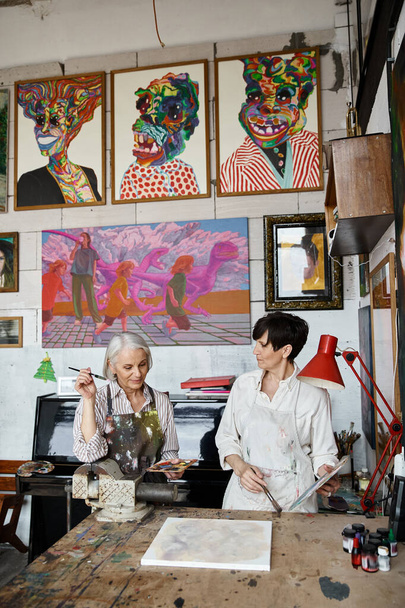 Dwie kobiety podziwiają obrazy w przytulnym studio sztuki. - Zdjęcie, obraz