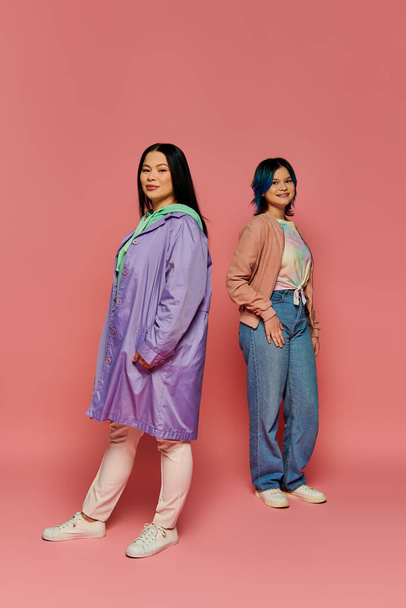 Una madre asiatica e sua figlia adolescente si trovano l'una accanto all'altra in abiti casual su uno sfondo rosa. - Foto, immagini