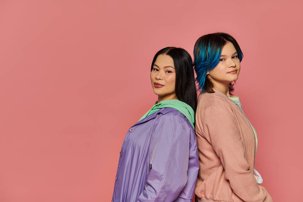 A stylish Asian mother and her teenage daughter, both with vibrant blue hair, pose together on a pink studio background. - Photo, Image