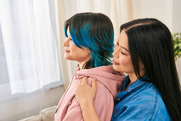 Una madre y una hija adolescente, de ascendencia asiática, se mantienen estrechamente unidas en un atuendo casual, compartiendo un momento de conexión en casa. - Foto, imagen