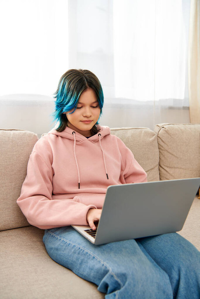 Ein asiatisches Mädchen mit blauen Haaren sitzt auf einer Couch und tippt auf einem Laptop, während sie Zeit zu Hause verbringt. - Foto, Bild
