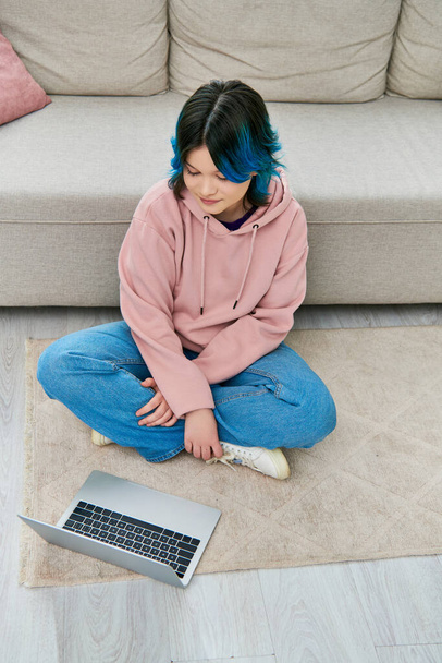 Una chica con el pelo azul se sienta al lado de un portátil en el suelo, profundamente en el pensamiento - Foto, Imagen