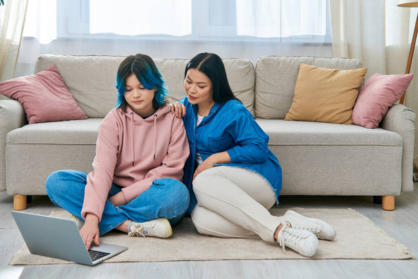 Äiti ja hänen teini-ikäinen tyttärensä, rento puku, istuu lattialla, täysin mukana kannettavan tietokoneen näytöllä. - Valokuva, kuva