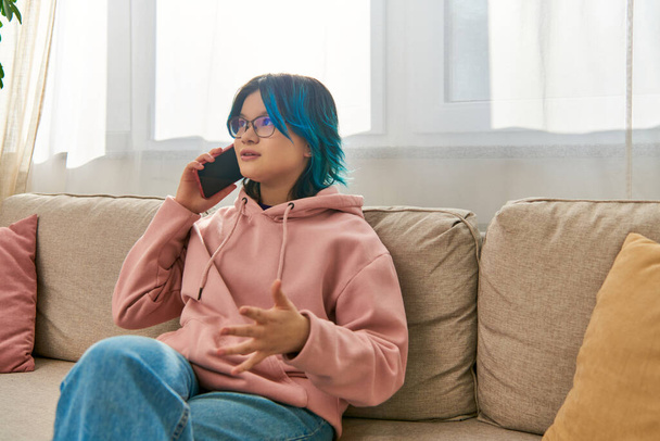Uma menina asiática com cabelo azul sentar em um sofá, falando em um telefone celular juntos. - Foto, Imagem