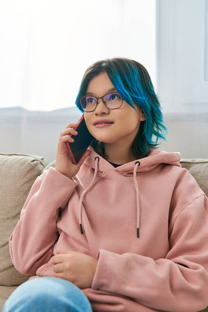 Un'adolescente si siede su un divano, impegnata in una conversazione su un telefono cellulare. - Foto, immagini