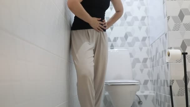 Kobieta stoi we współczesnej łazience, ściskając żołądek w dyskomforcie, sugerując, że może odczuwać ból brzucha lub skurcze. Środowisko jest czyste i dobrze oświetlone, pokazując - Materiał filmowy, wideo