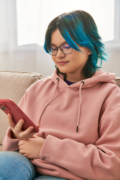 Una ragazza asiatica capelli blu, sedersi comodamente su un divano, godendo di un momento di connessione - Foto, immagini