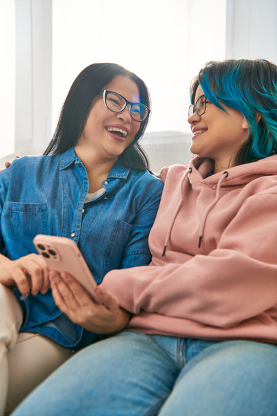 Asiatische Mutter und Teenager-Tochter in Freizeitkleidung sitzen zusammen auf einer Plüschcouch und teilen einen Moment der Nähe. - Foto, Bild