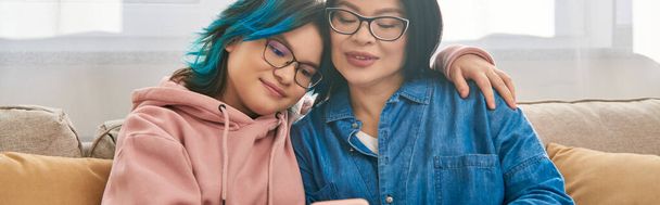 Een Aziatische moeder en haar tienerdochter, in casual kleding, ontspannen en bonding op de top van een comfortabele bank thuis. - Foto, afbeelding