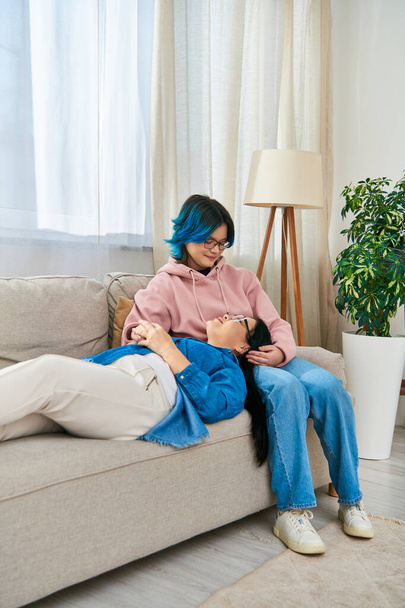 A mother and daughter, both Asian, relax together on a couch at home. - Photo, Image