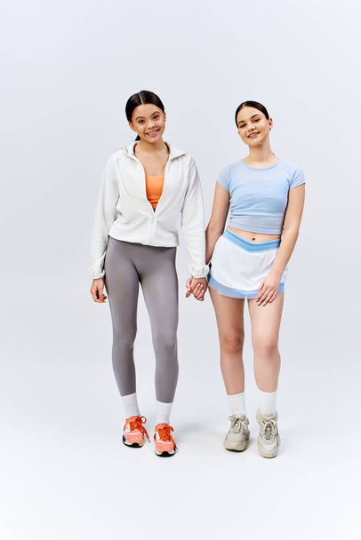 Dwie ładne, brunetka nastolatki stoją obok siebie, trzymając się za ręce w pokaz przyjaźni na szarym tle studio. - Zdjęcie, obraz