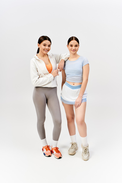 Dvě hezké, brunetky dospívající dívky ve sportovním oblečení stojí bok po boku ve studiu, vyzařuje důvěru a přátelství. - Fotografie, Obrázek