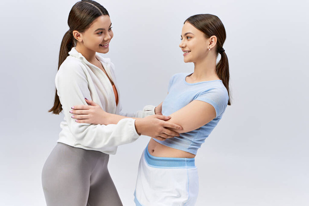 Zwei hübsche Mädchen im Teenageralter, brünett und in sportlicher Kleidung, stehen nebeneinander in einem Studio vor grauem Hintergrund. - Foto, Bild