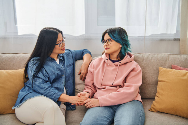 Uma mãe asiática e sua filha adolescente em roupas casuais se envolvem em uma conversa profunda enquanto se sentam em um sofá aconchegante. - Foto, Imagem