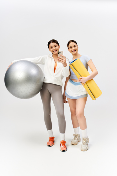 Two pretty and brunette teenage girls in sportive attire stand side by side in a studio, showcasing their friendship. - Photo, Image