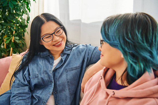 Aziatisch moeder en tienerdochter deel te nemen in oprechte gesprek op een gezellige bank thuis, het creëren van een warme en liefdevolle sfeer. - Foto, afbeelding
